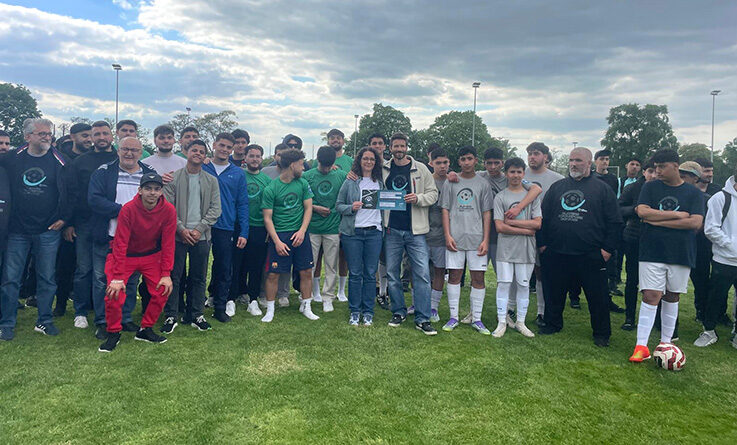 Eine große Gruppe, darunter Fußballspieler in Sportkleidung und andere in Freizeitkleidung, posieren nach dem Players for Purpose Cup gemeinsam auf einer Wiese. Einige Spieler halten eine Urkunde und einen Pokal für den 6. Platz und ein Preisgeld von 750 Euro in der Hand.